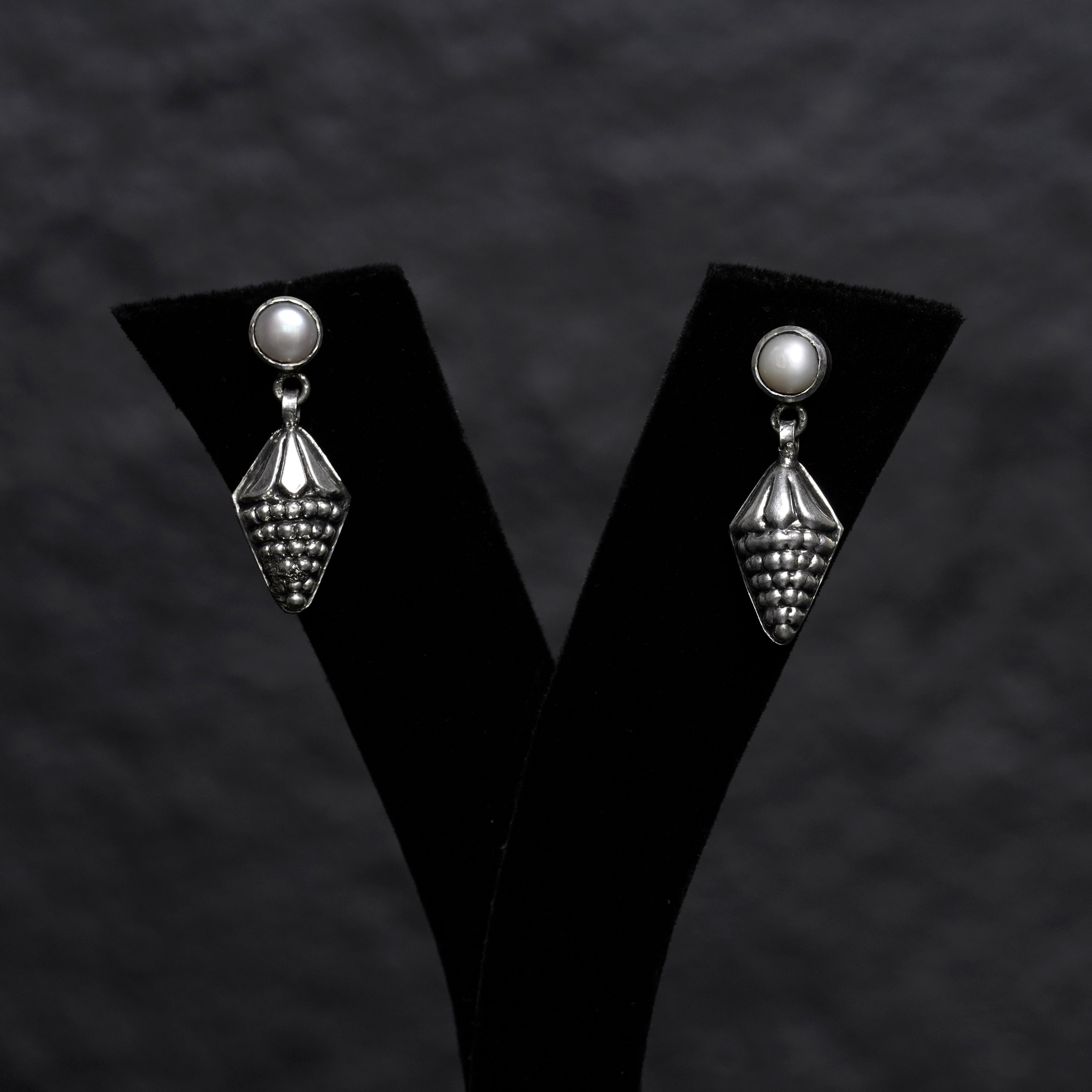 Pair of silver earrings on a black 'V' shaped stand against a dark textured background