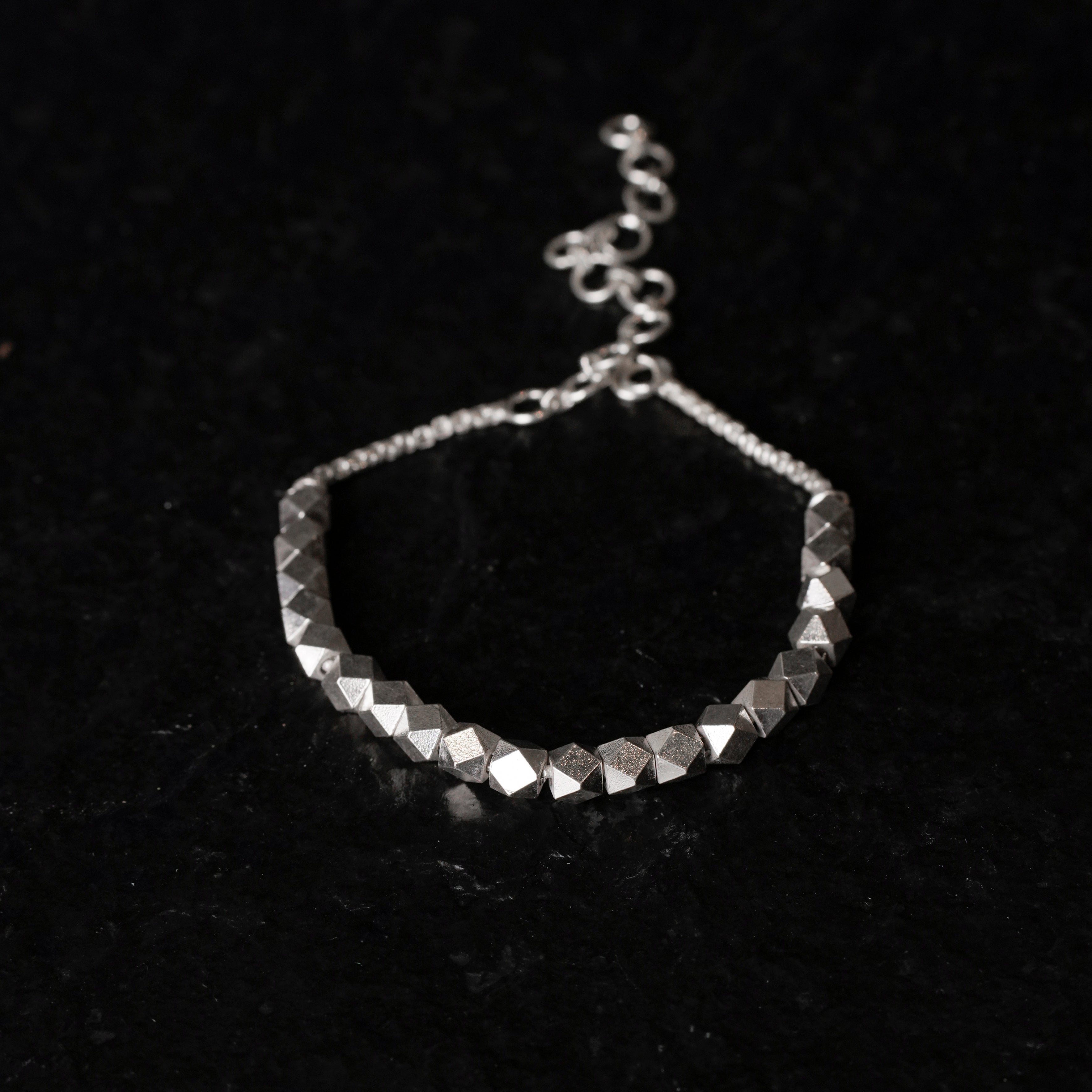 Silver beaded bracelet on a black textured background